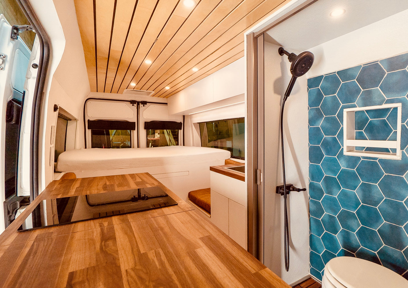 Spacious rv rental interior featuring a wood ceiling, integrated kitchen, bed, and a stylish blue-tiled shower.