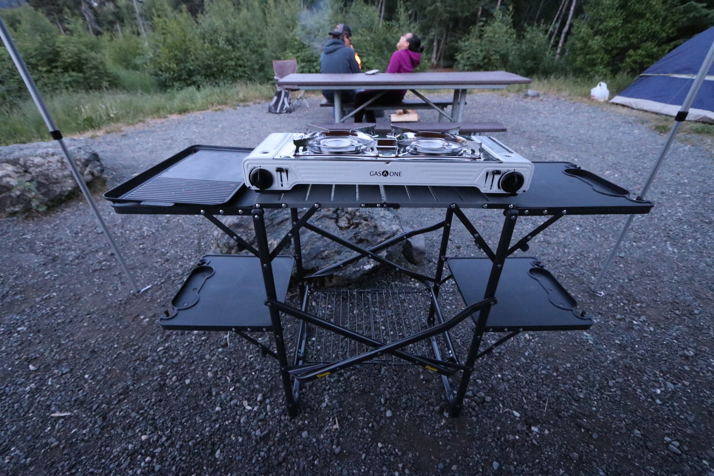 This portable camping kitchen with a Gas One stove is ideal for your RV rental adventure, with campers enjoying a fire.