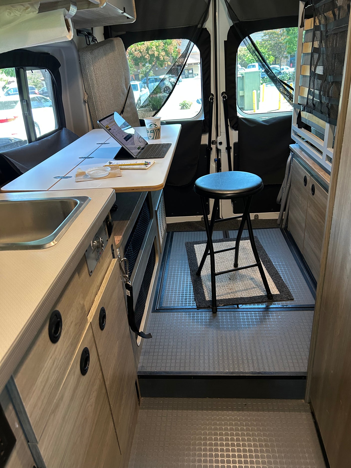 RV rental's compact interior features a versatile workspace with a laptop, a kitchen sink, and ample storage.