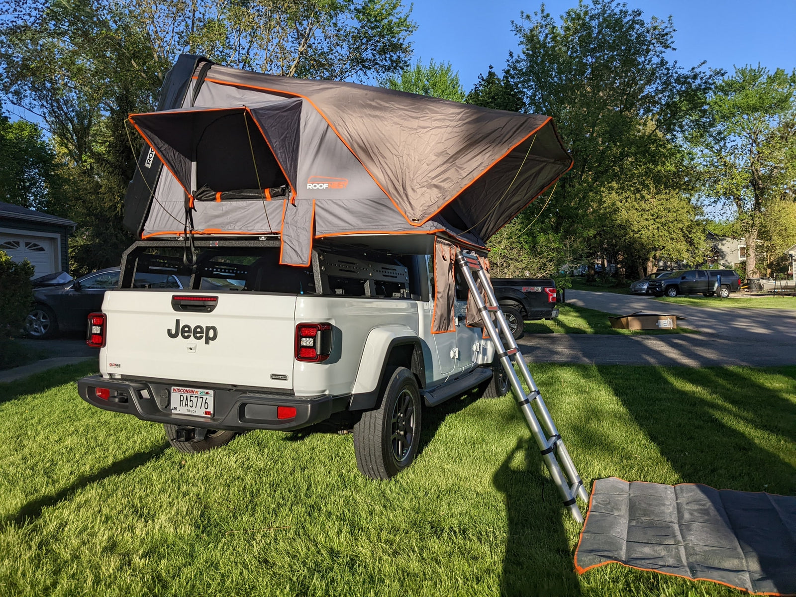 Setup for adventure: White Jeep Gladiator with a rooftop tent & ladder on a green lawn. Consider this unique rv rental for camping.|White Jeep Gladiator with rooftop tent & child climbing ladder