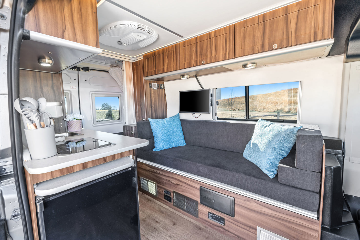 Experience comfort in this RV rental: full kitchen, cozy sofa, TV, and scenic window views for your road trip.