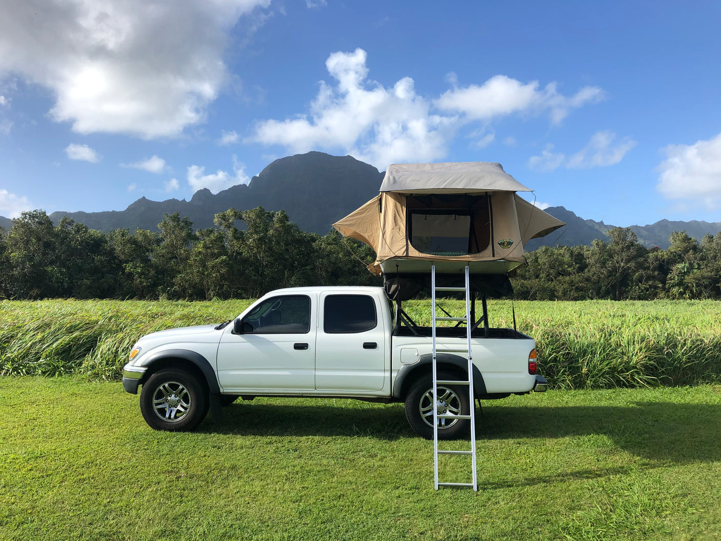 White truck with rooftop tent, ready for RV rental adventures. Camp in green fields with mountains in background.
