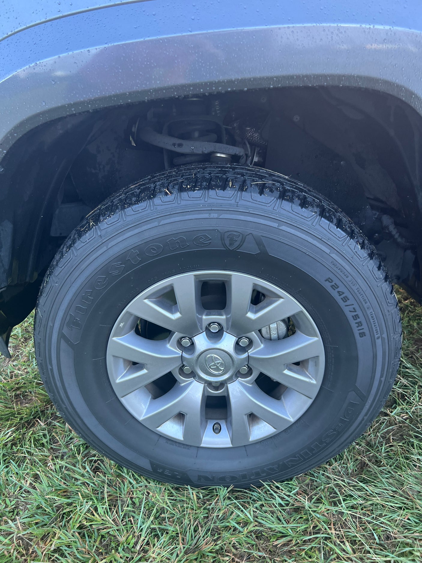 Firestone tire and Toyota wheel of a durable vehicle on wet grass, perfect for your next RV rental road trip.