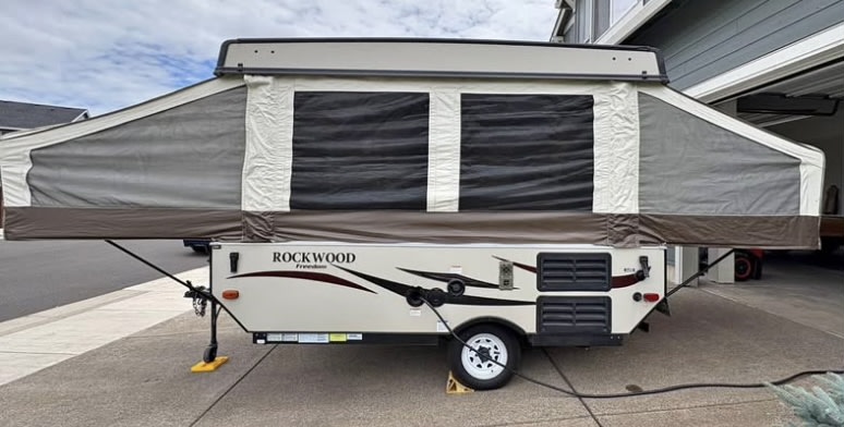showcasing its extended canvas and screened windows. Great for RV rental.|Interior of an RV rental: cozy pop-up camper with a bed