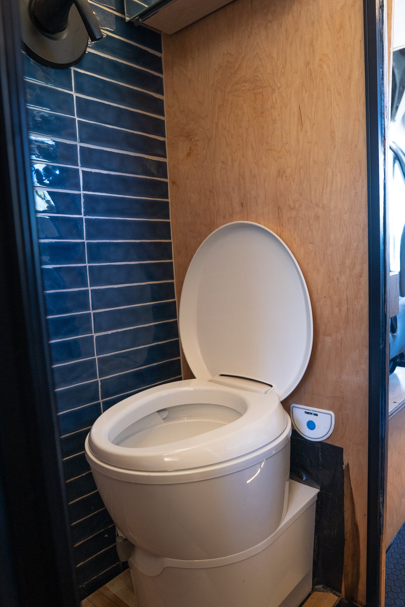 Functional RV rental wet bath with a white Thetford toilet (lid open), blue tiled shower, and wood paneling.