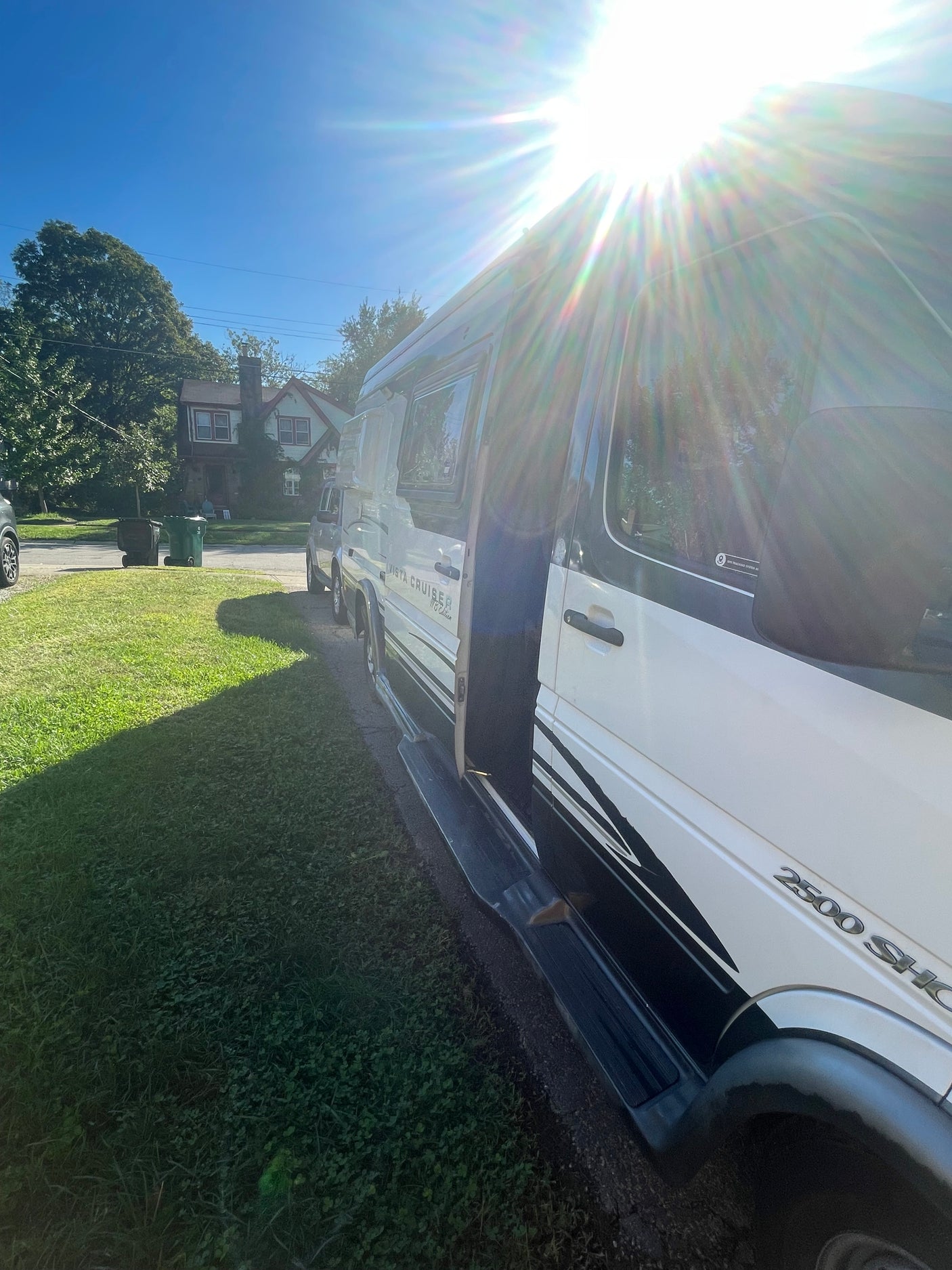 An RV rental camper van, white and black Vista Cruiser, parked in a sunny residential area with its side door open.