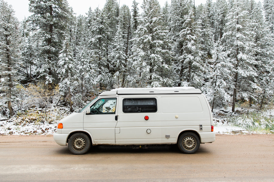 White camper van RV rental parked on a snowy forest road. Ready for your winter adventure.