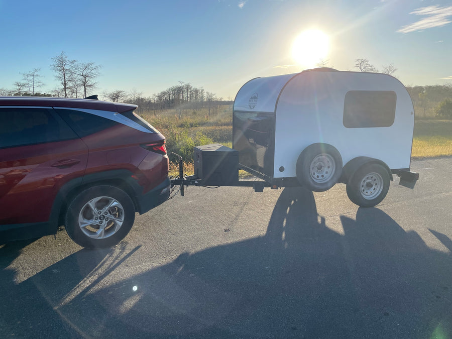 perfect for outdoor travel. Parked on an asphalt path with a natural setting.|Red SUV towing a teardrop camper (RV rental) on an asphalt road at sunset. Ideal for outdoor adventures and camping.|Rustic Trail Teardrops RV rental: a compact