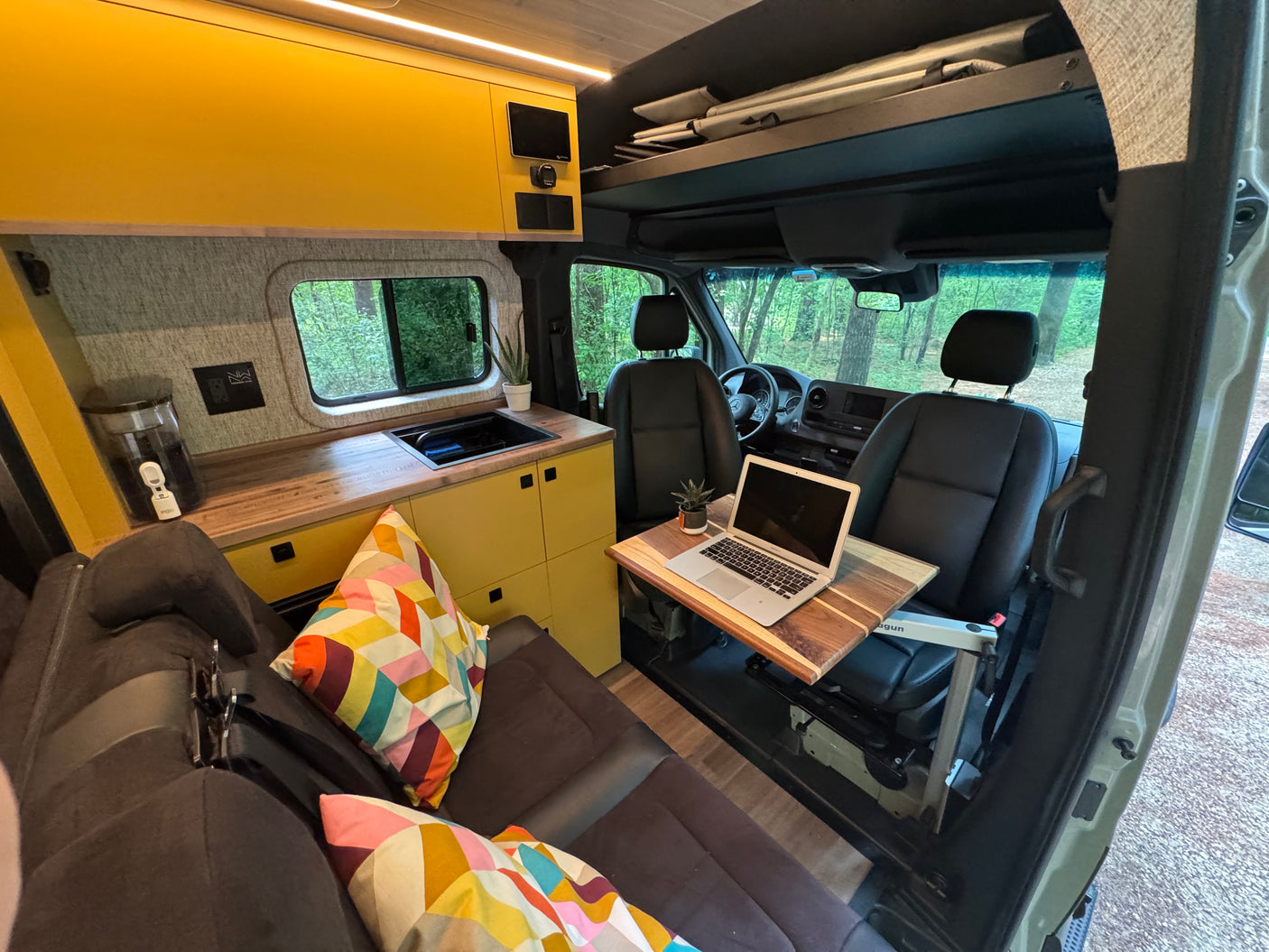 Explore this RV rental's versatile interior: a bright kitchenette, cozy seating, & mobile desk with laptop. Perfect for van life adventures.