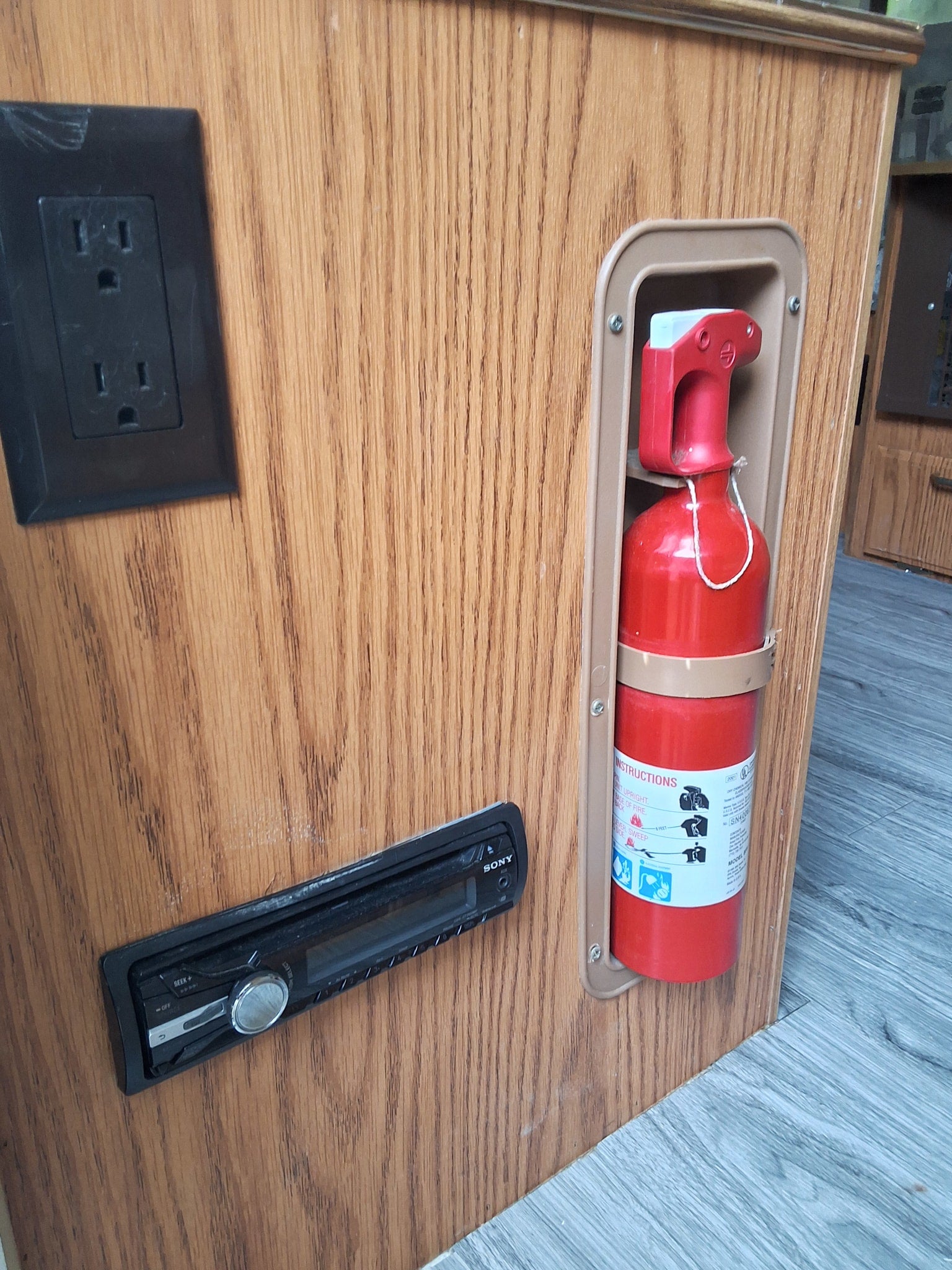 RV rental interior featuring a power outlet, Sony stereo, and an essential fire extinguisher mounted on wood paneling.