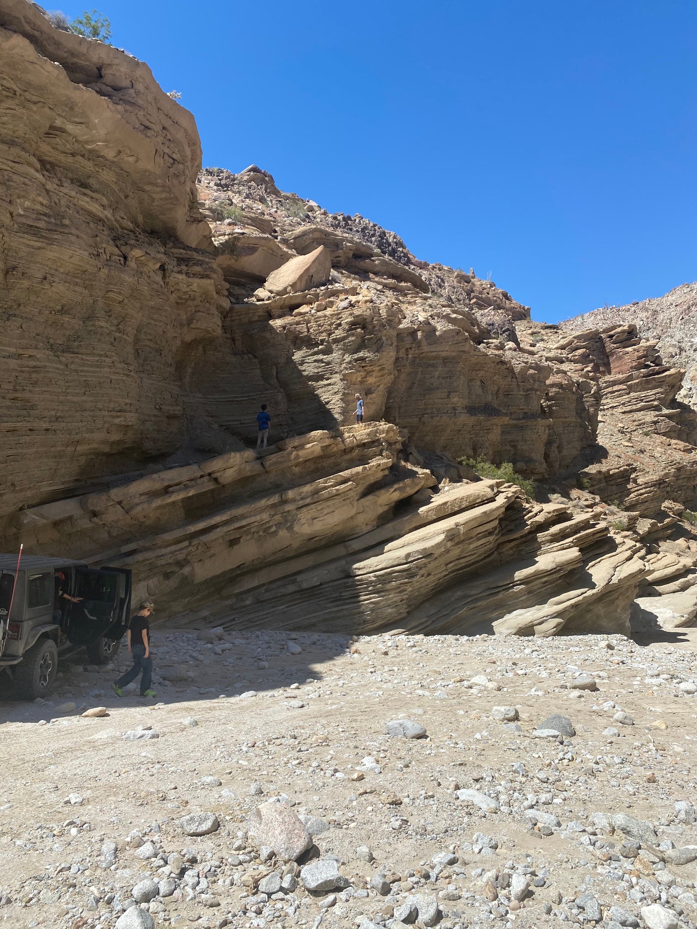 Off-roading in a rugged desert canyon with layered rock walls, a Jeep, and explorers. Imagine this adventure with an RV rental!