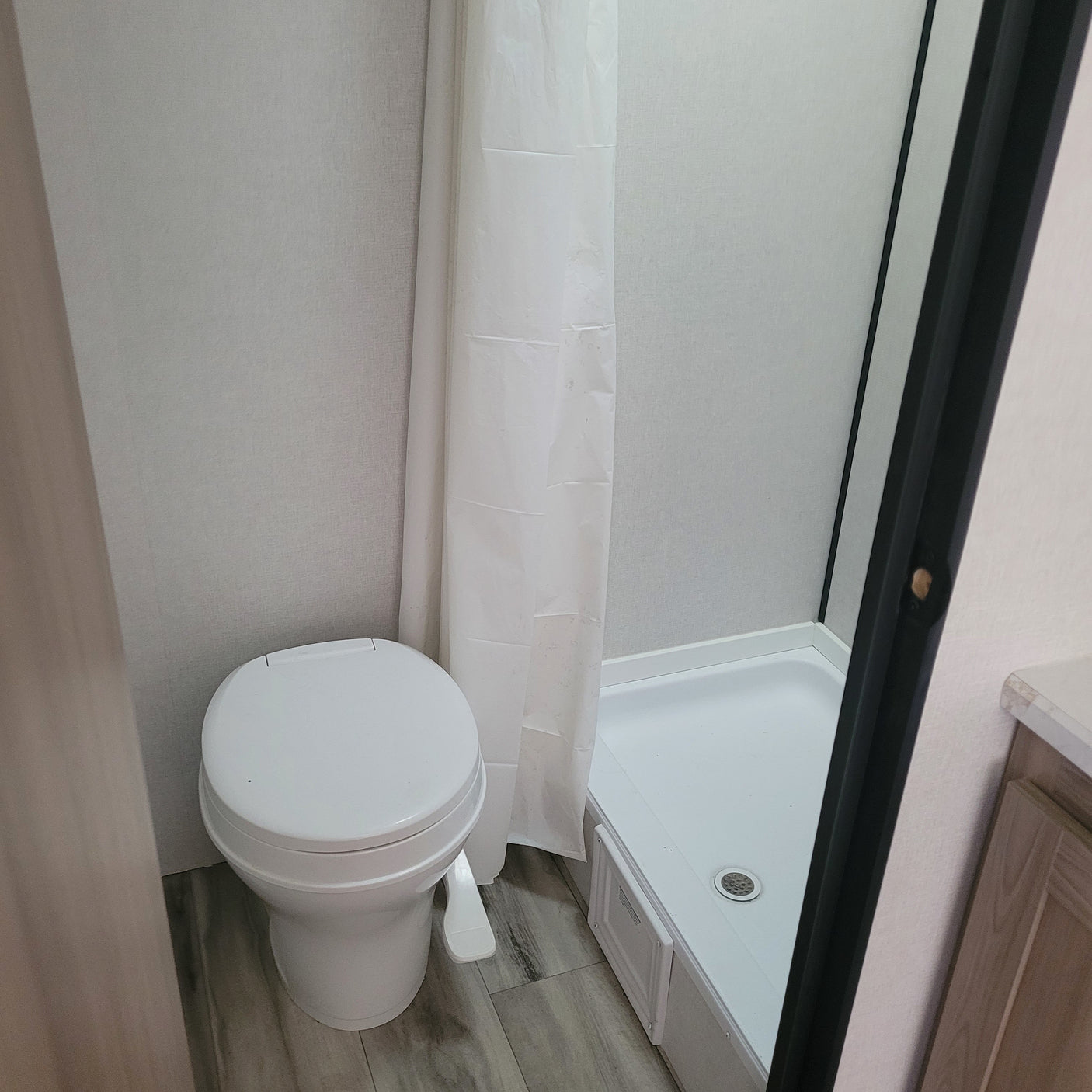 Compact RV rental bathroom featuring a white toilet, shower with a curtain, and a modern wood-look floor.