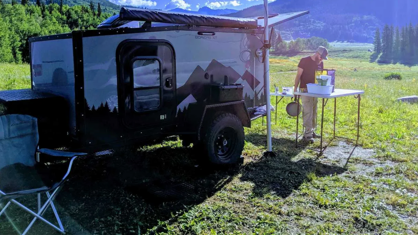 Enjoy scenic outdoor adventure with an RV rental. Man washing dishes next to an off-road teardrop camper in mountains.