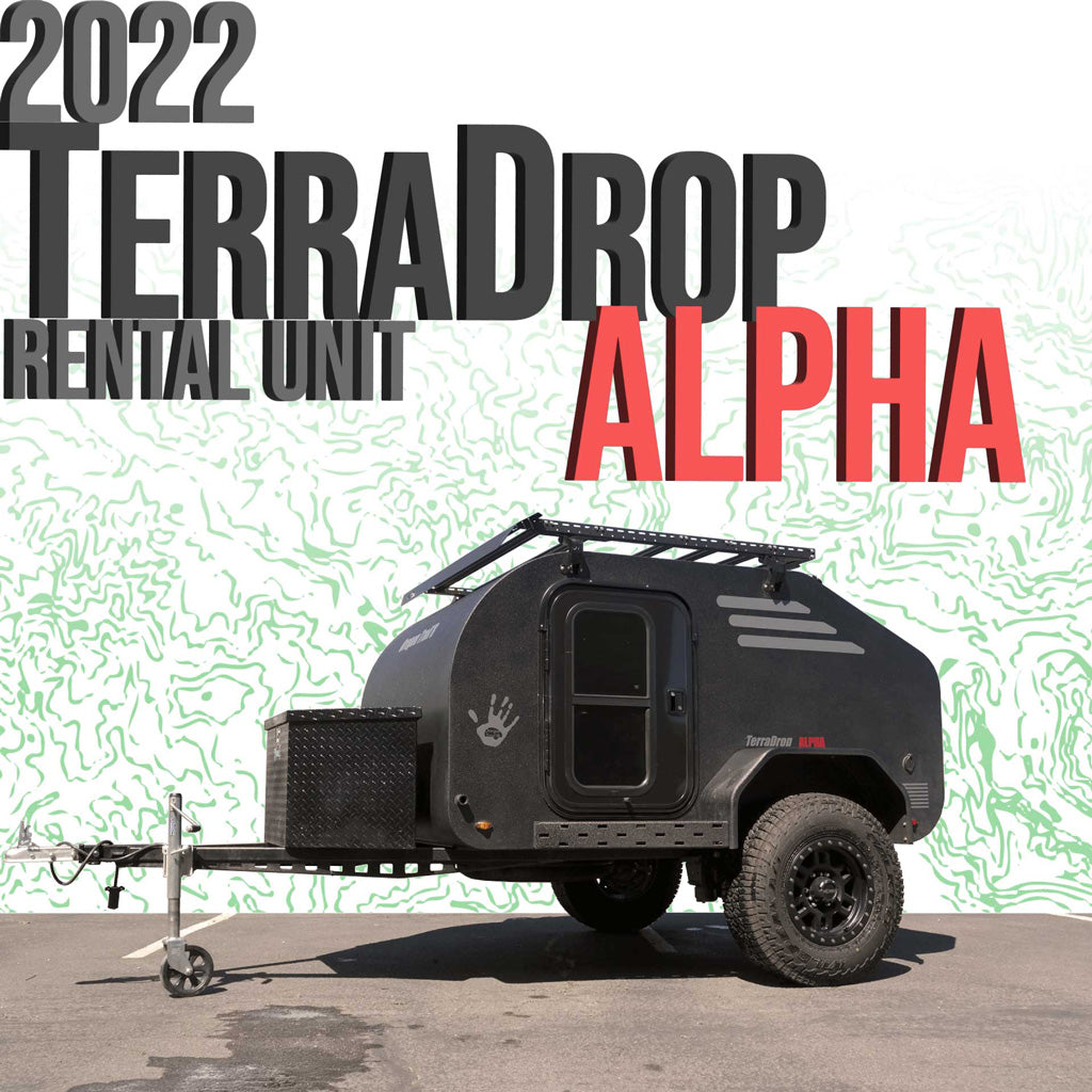This 2022 TerraDrop Alpha teardrop RV rental unit is a black trailer with off-road tires and a roof rack, parked on asphalt.