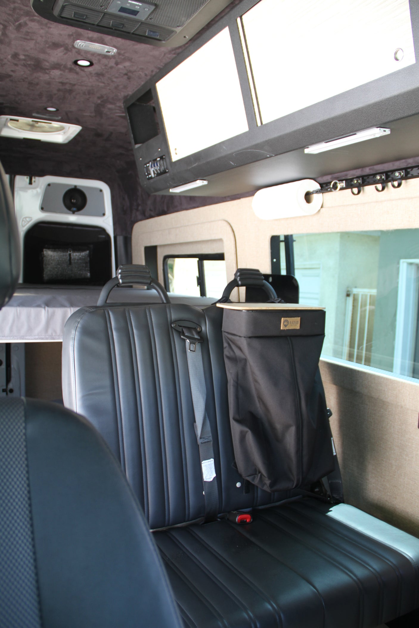 RV rental interior: black leather seats, rear bed, and overhead storage, offering comfort for your travels.