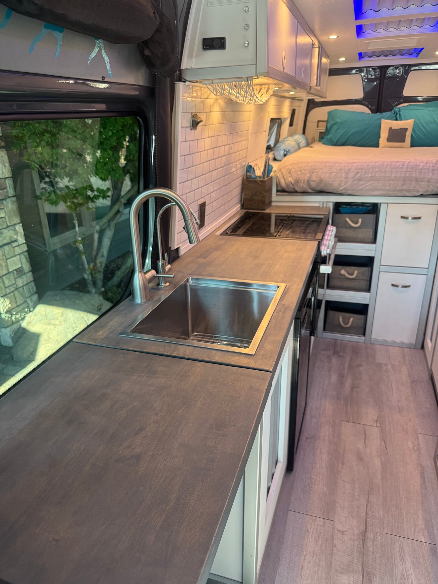 RV rental interior features a sleek kitchen with sink & cooktop, elevated bed, and integrated storage, showcasing efficient design.