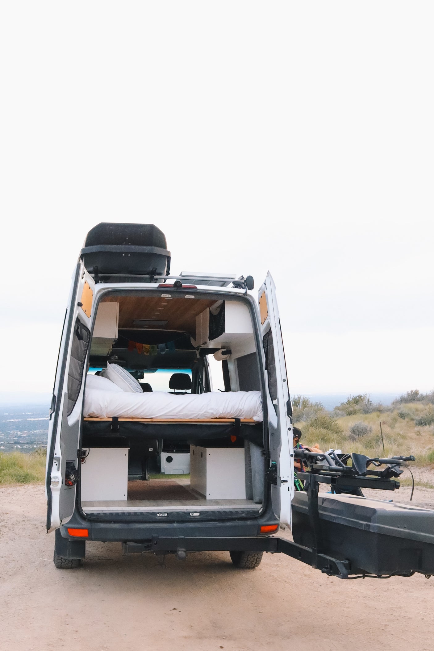 Rear view of a fully equipped camper van rv rental with open doors, revealing a cozy bed & storage. Perfect for a scenic road trip adventure!