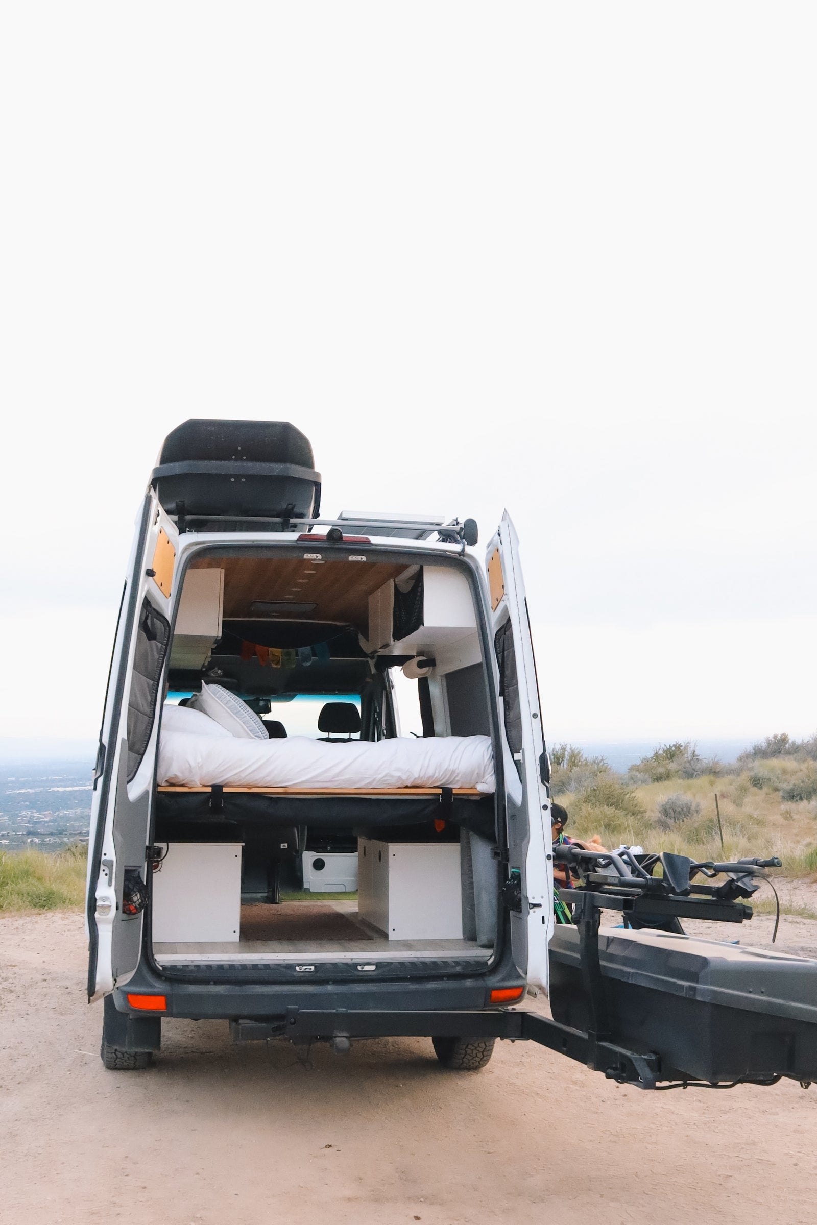 Rear view of a fully equipped camper van rv rental with open doors, revealing a cozy bed & storage. Perfect for a scenic road trip adventure!