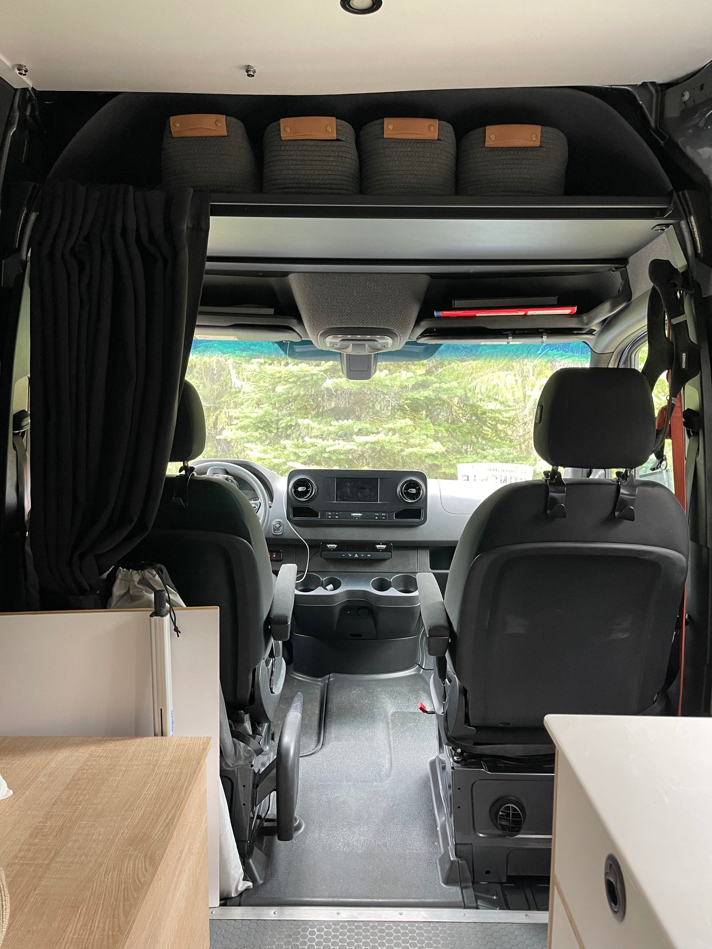 Interior of an rv rental camper van, showcasing the front cab, dashboard, seats, and overhead storage bins.