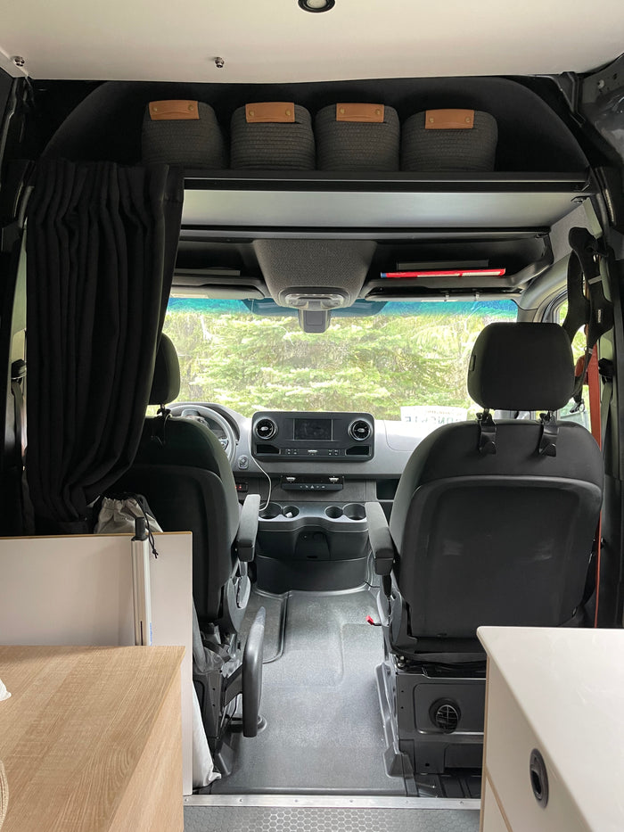 Interior of an rv rental camper van, showcasing the front cab, dashboard, seats, and overhead storage bins.