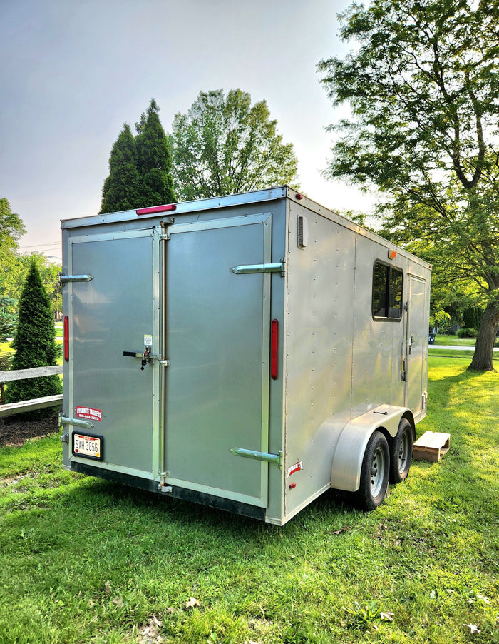 and warm wood paneling.|Unique RV rental: a converted silver cargo trailer camper with an open side door & propane tank