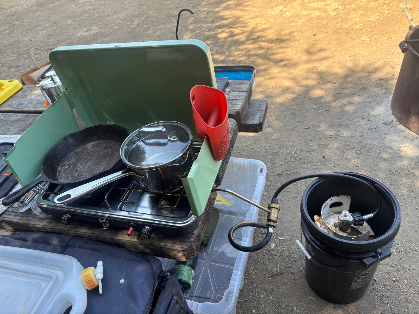 Outdoor cooking at your RV rental: a portable propane stove with a cast iron pan & pot, plus a water jug, on a picnic table.