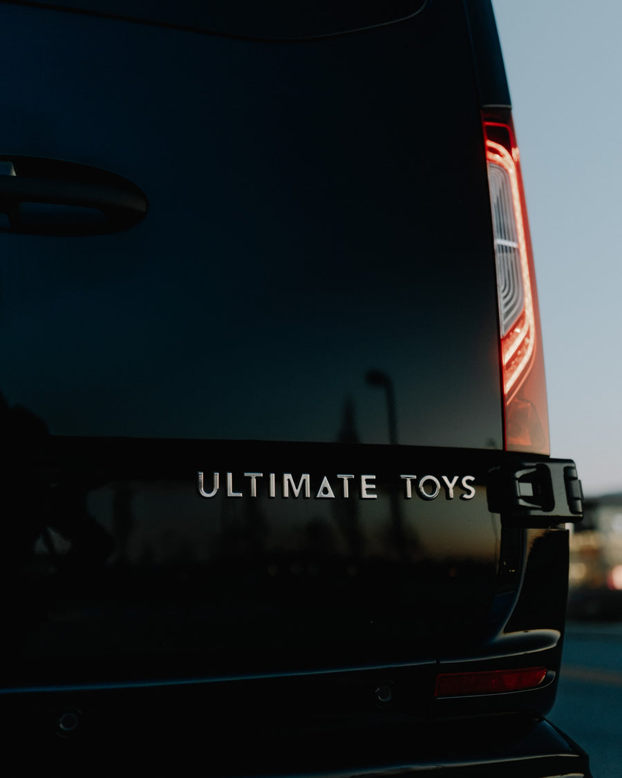 Rear of a dark "ULTIMATE TOYS" luxury custom van with a bright vertical taillight, perfect for rv rental.