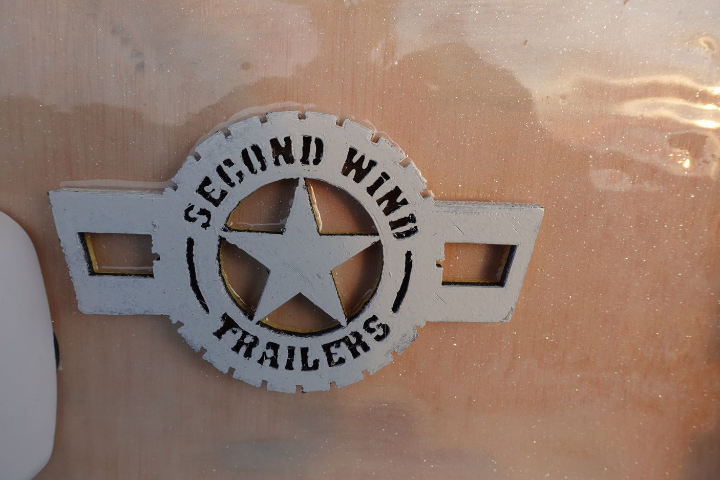 White & black 'Second Wind Trailers' logo with a star, set in clear resin on an RV panel, ready for rv rental.