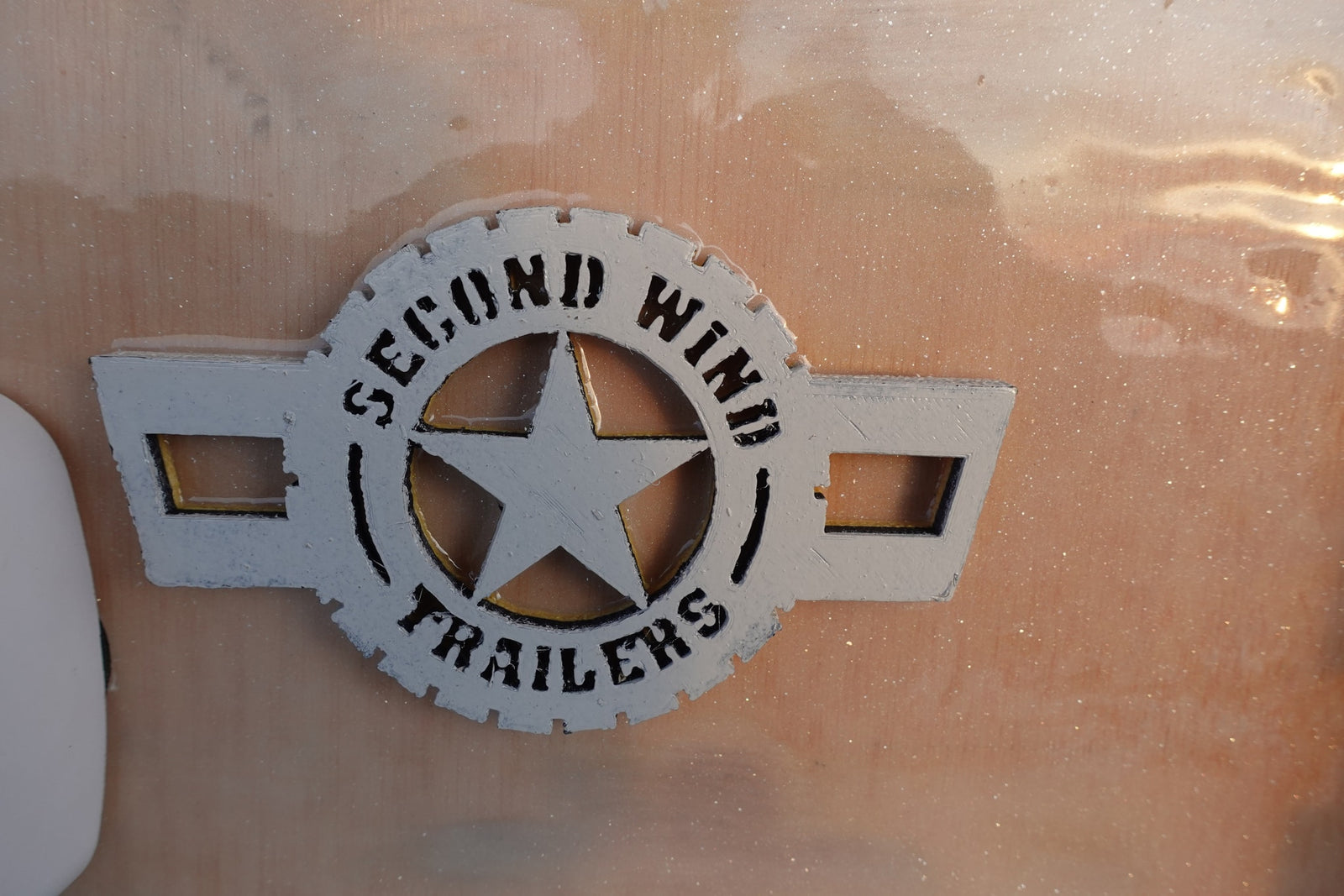 White & black 'Second Wind Trailers' logo with a star, set in clear resin on an RV panel, ready for rv rental.