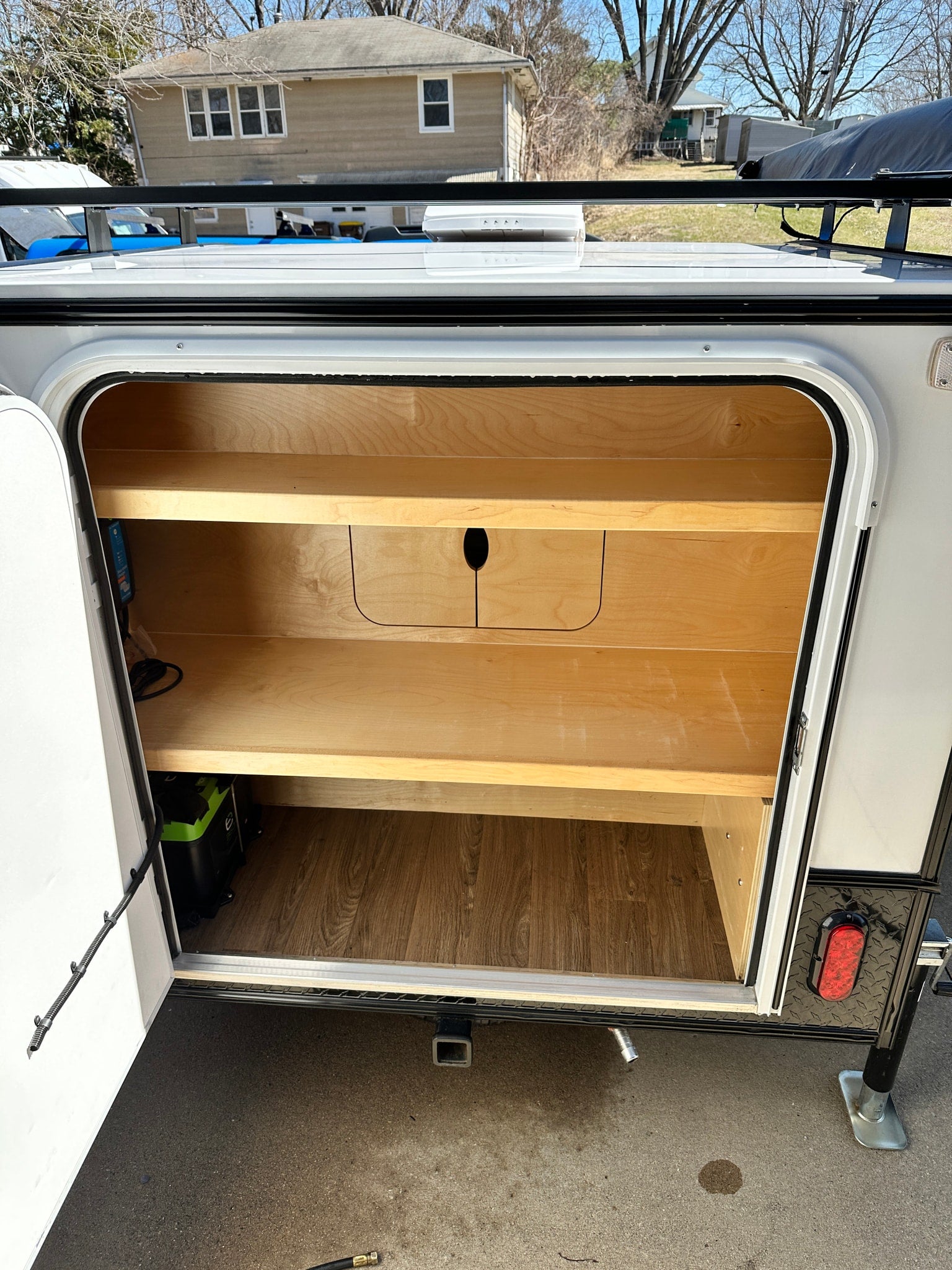 set up with an awning outside a home garage on a sunny day.|RV rental: Compact white & black camper side