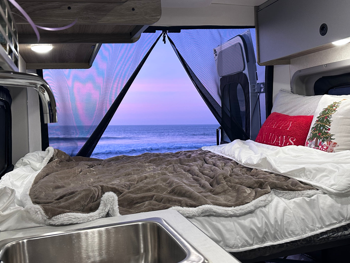 Enjoying a serene ocean sunset from a comfy RV rental bed, complete with holiday pillows.