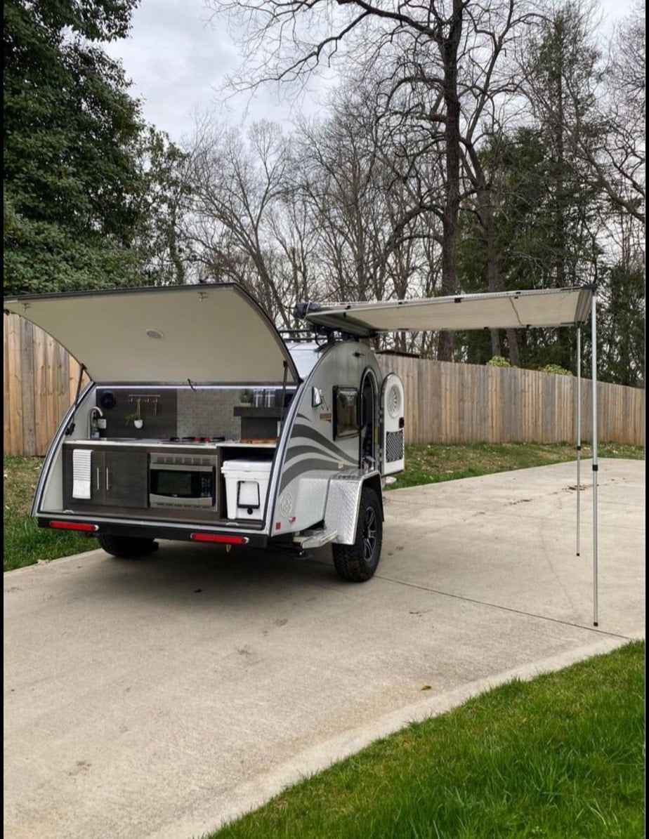 An rv rental compact teardrop trailer with an outdoor kitchen setup and side awning extended, ready for travel.