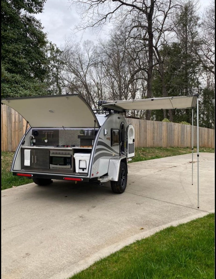 An rv rental compact teardrop trailer with an outdoor kitchen setup and side awning extended, ready for travel.