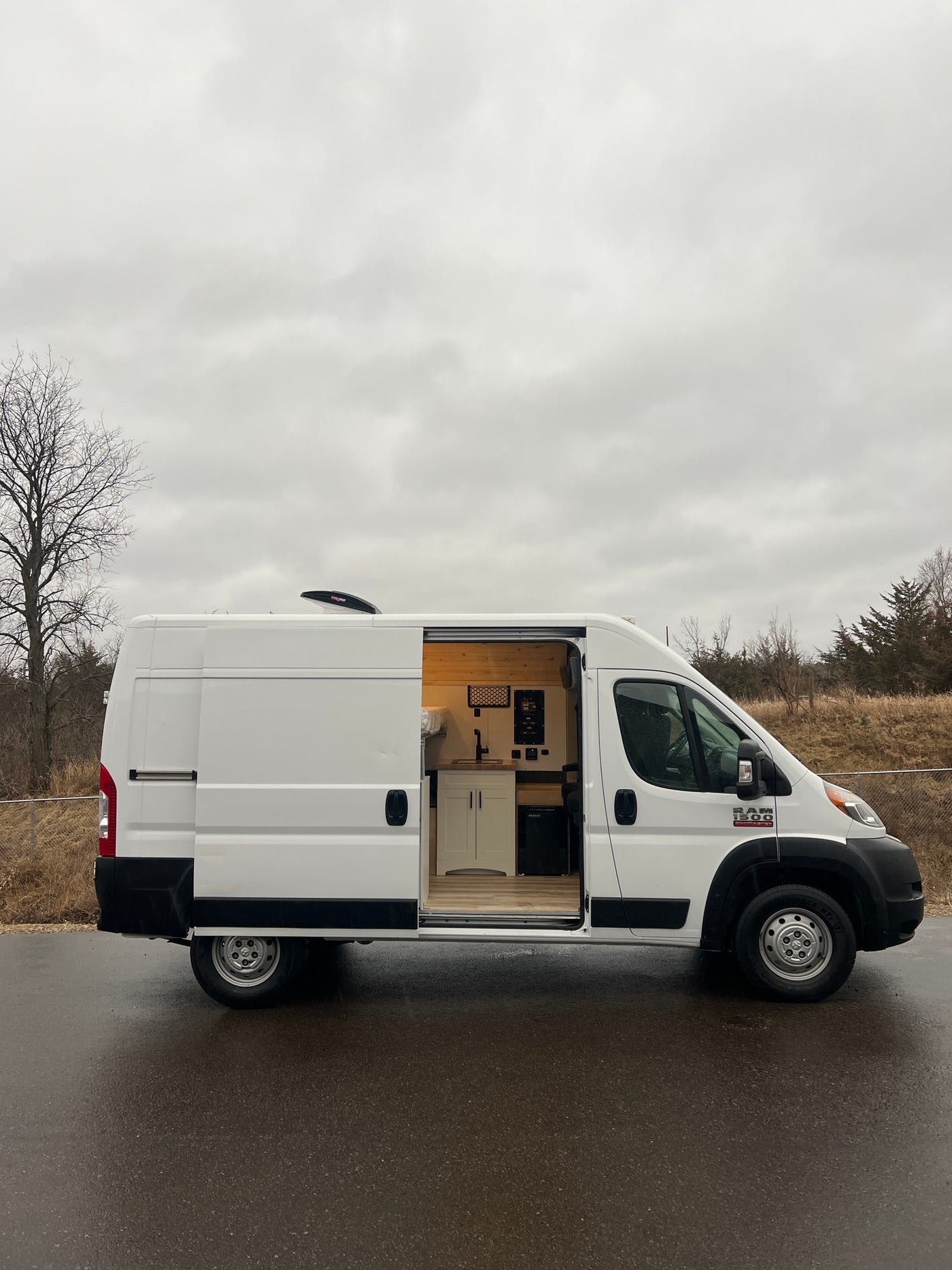 White camper van conversion with open side door revealing a custom kitchen and bed. Ideal RV rental for mobile adventures.|Explore this RV rental's well-designed camper van interior featuring a comfortable bed — photo 1