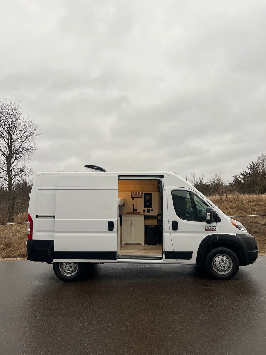 White camper van conversion with open side door revealing a custom kitchen and bed. Ideal RV rental for mobile adventures.