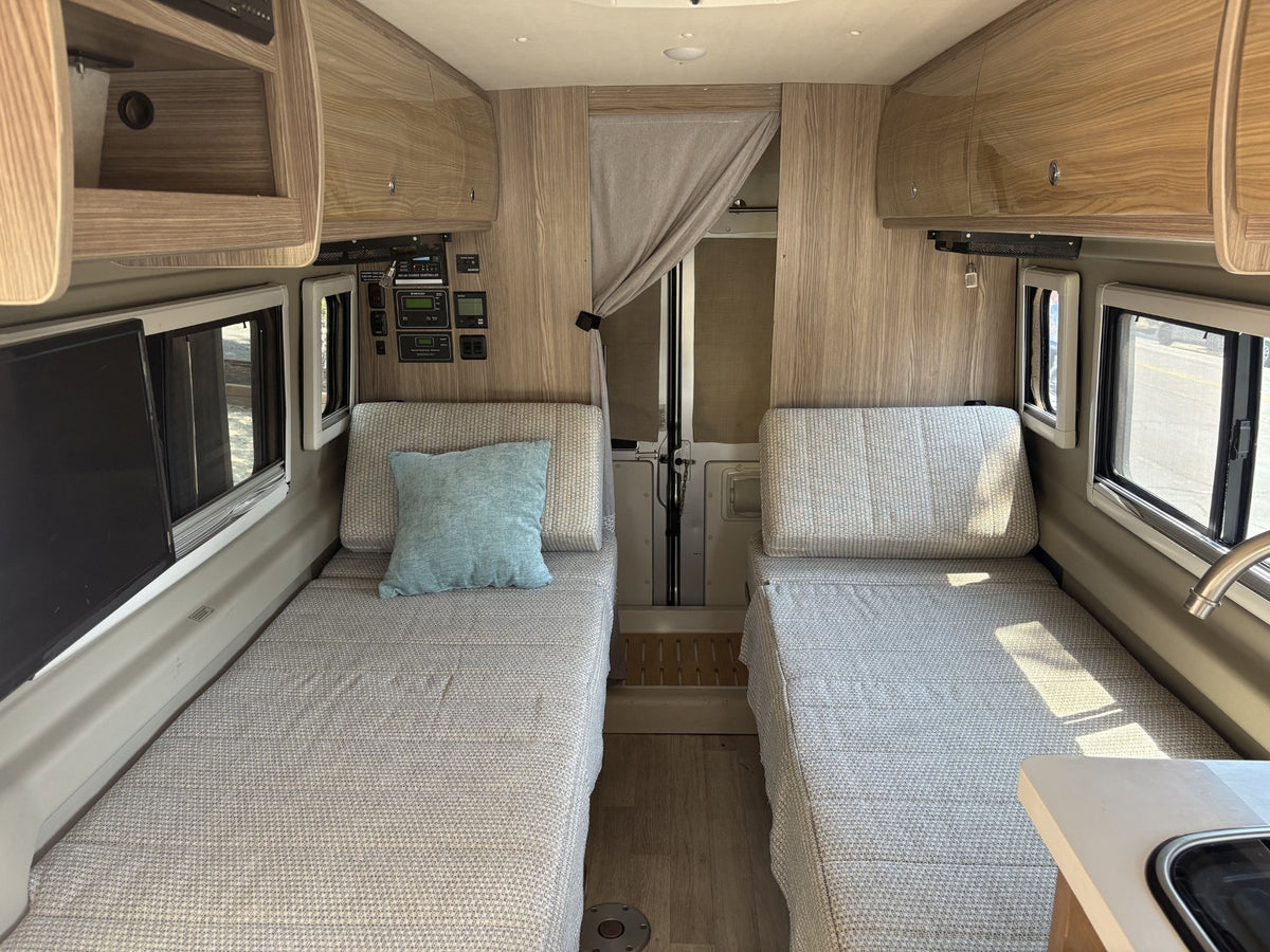 RV rental interior features twin beds with patterned bedding, overhead storage, and control panels for your journey. — photo 8