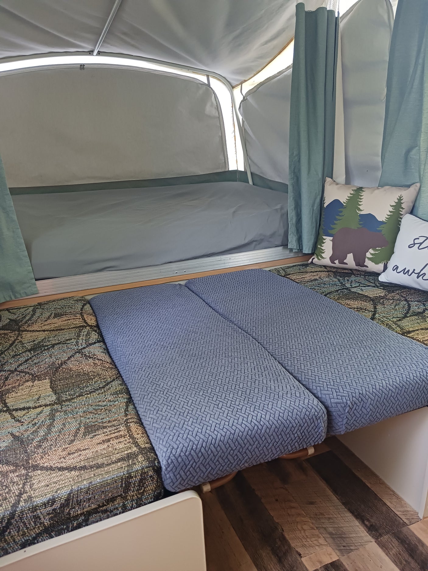 RV rental interior: a comfy bed, blue cushions, and a bear pillow in a cozy pop-up camper.