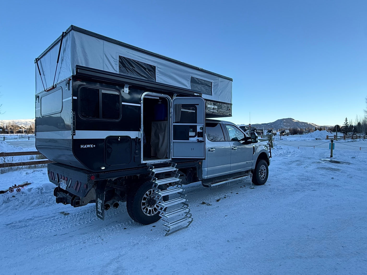 Rugged Four Wheel Hawk+ truck camper RV rental, pop-top extended on a snowy day. Steps deployed for winter adventure.