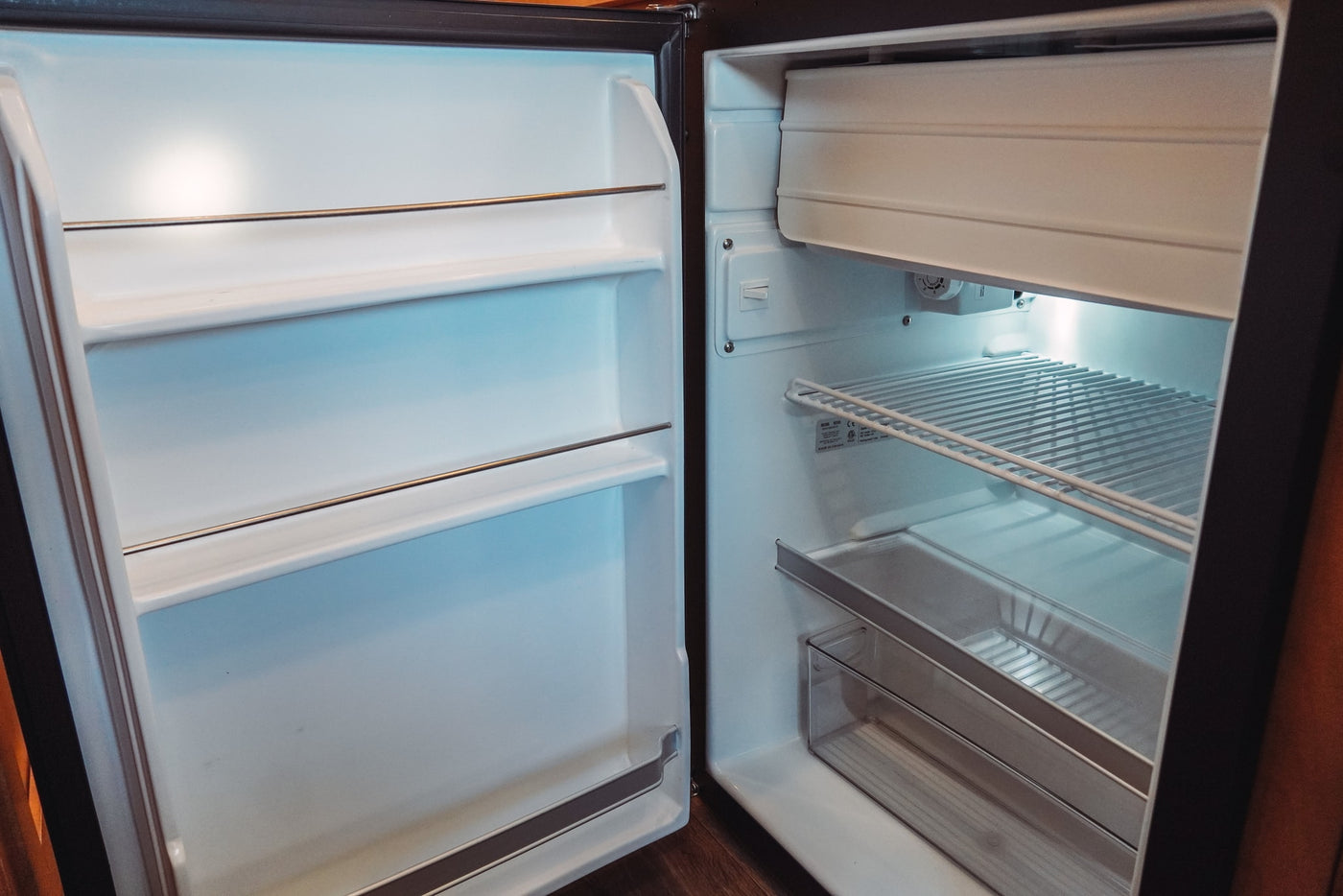 This open, clean, and empty mini-fridge in an RV rental features wire shelves, a freezer, and is ready for your food. — photo 20