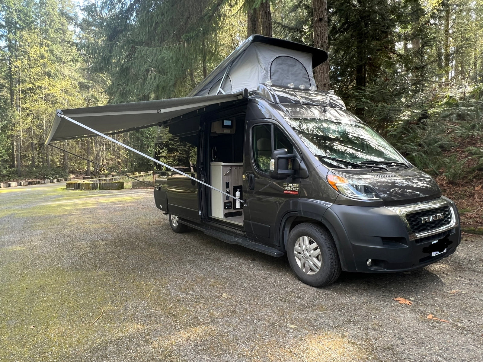 Pop-top RAM camper van, an ideal rv rental, parked with awning extended in a serene forest campground. Explore nature!