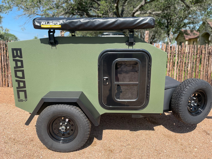 This rugged olive-green BADAC SS-7 off-road RV rental trailer, equipped with an Alltop awning, is ready for your adventure.