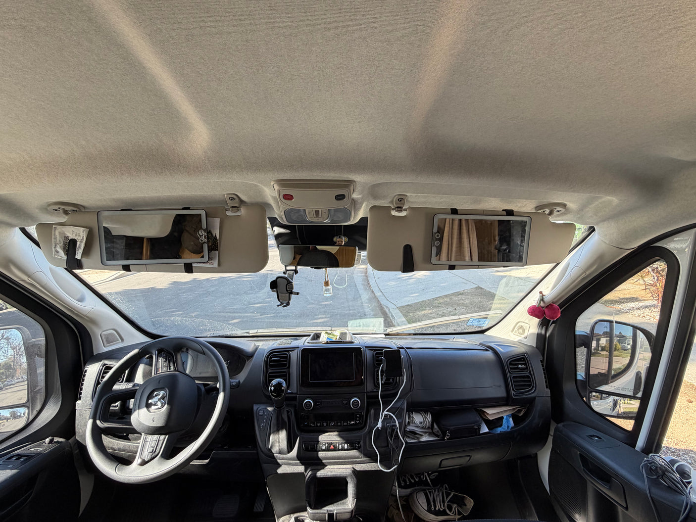 Inside an RV rental: a full view of the front cabin, dashboard, and steering wheel, with sun visors down and personal items visible.