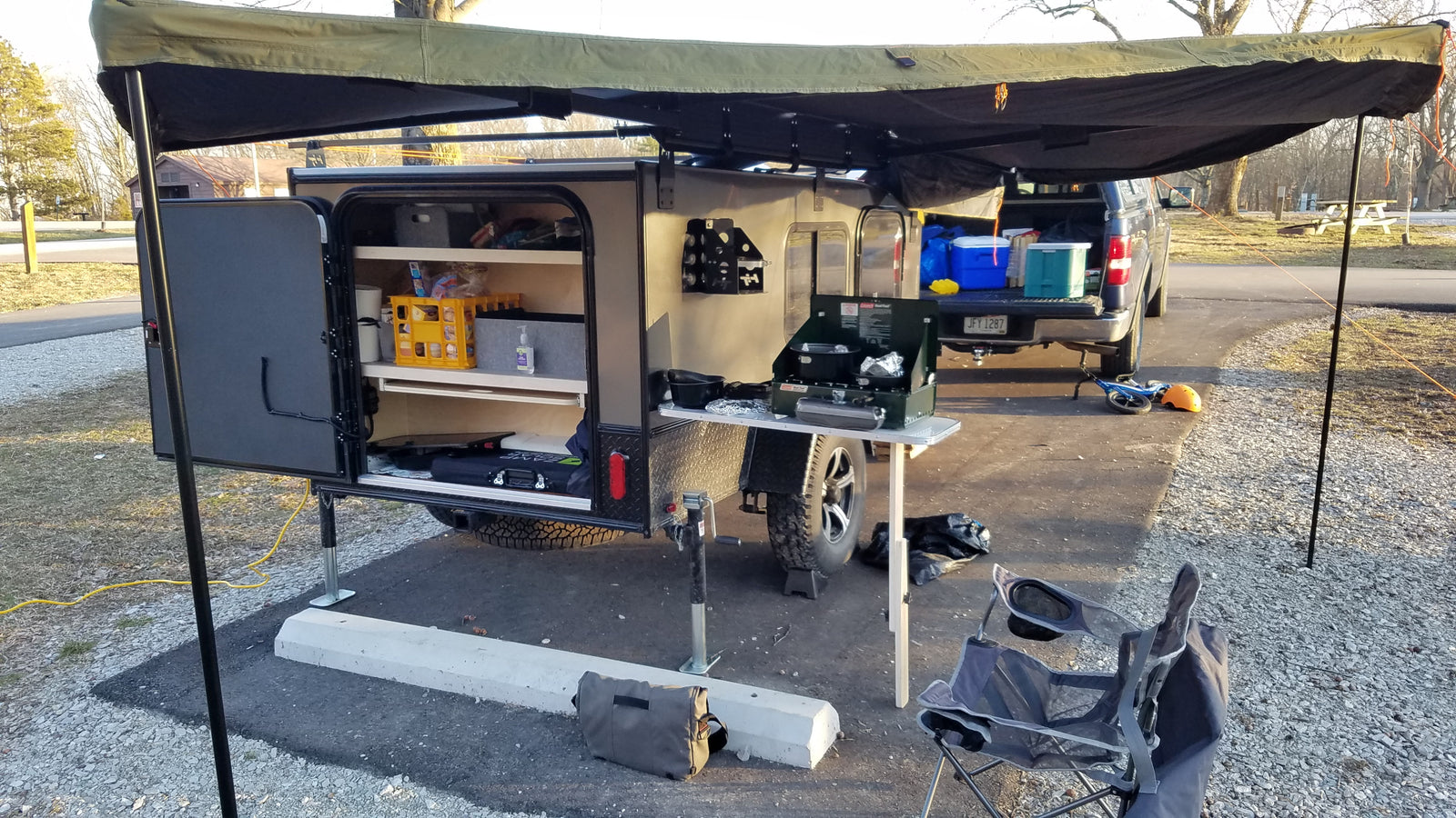 RV rental: Compact camper with outdoor kitchen, awning, and camping gear set up at a scenic campsite. Ready for adventure!