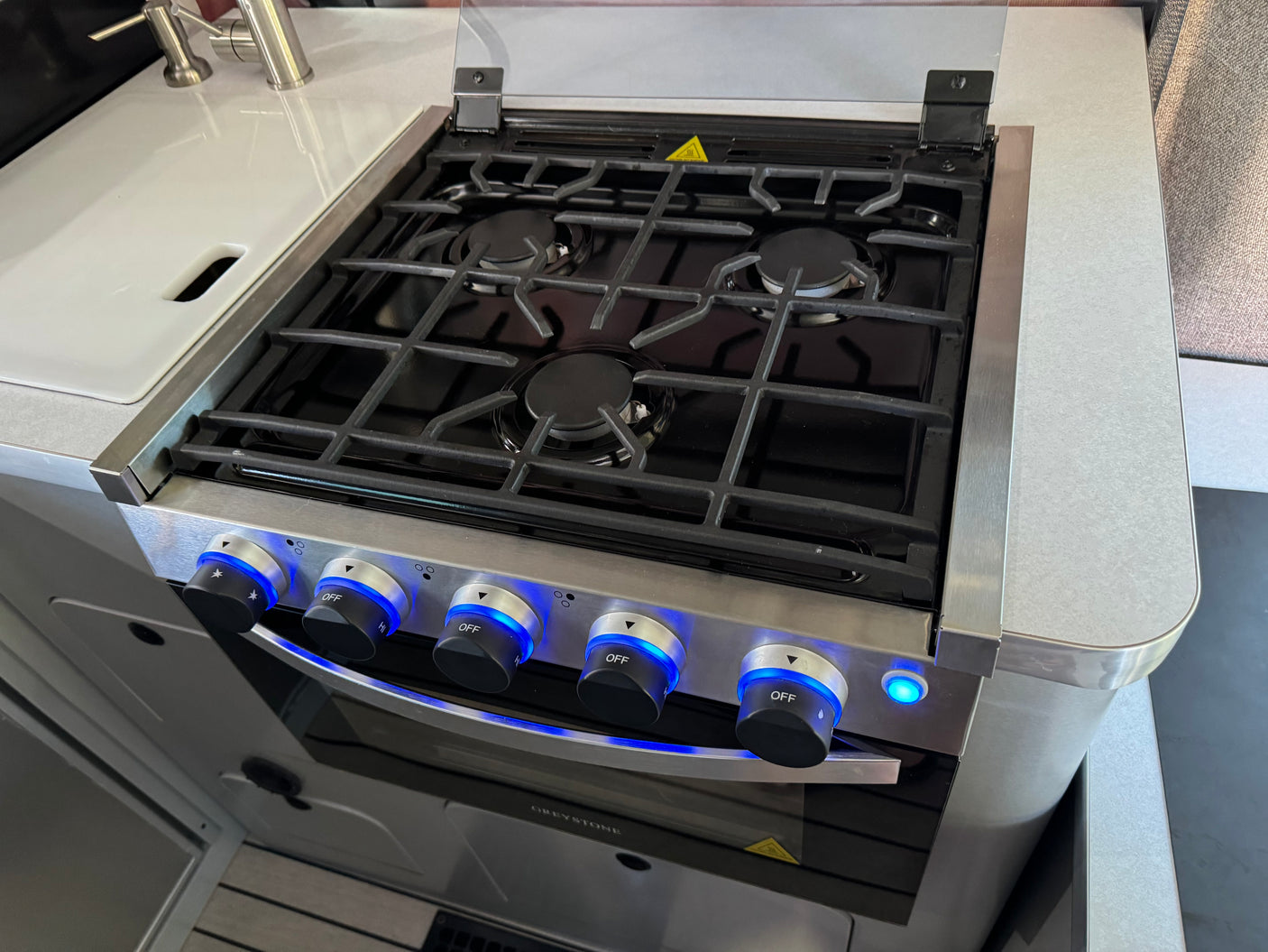 Modern RV rental kitchen with a sleek gas stove, oven below, and three burners with cast iron grates. Knobs feature blue LED lights.