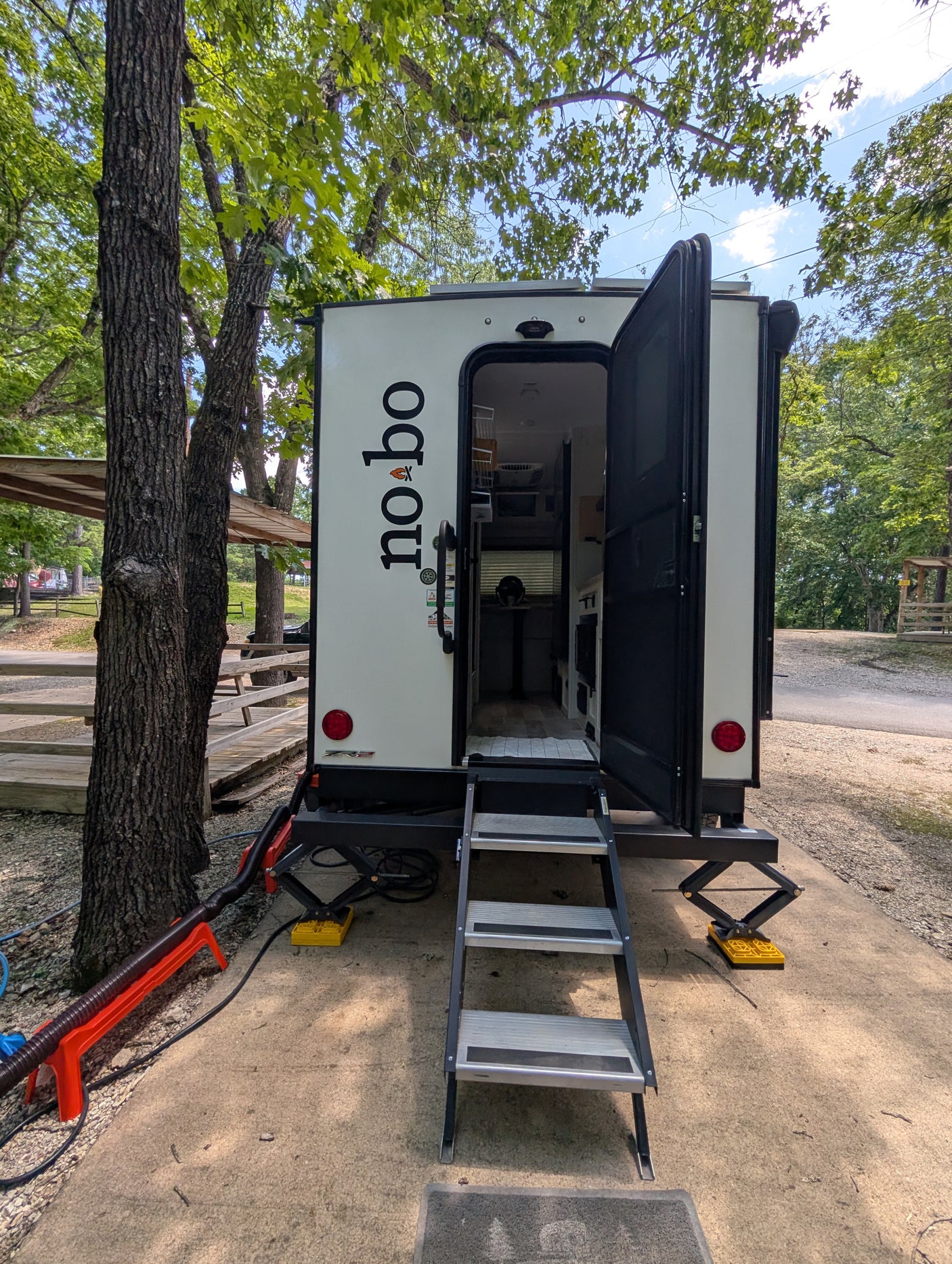 This white "no bo" travel trailer rv rental is set up in a wooded campground, with its door open and steps extended.