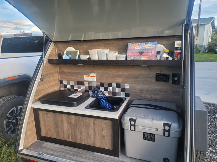 Teardrop RV rental kitchen setup with portable stove, sink, and cooler, perfect for camping and outdoor cooking.