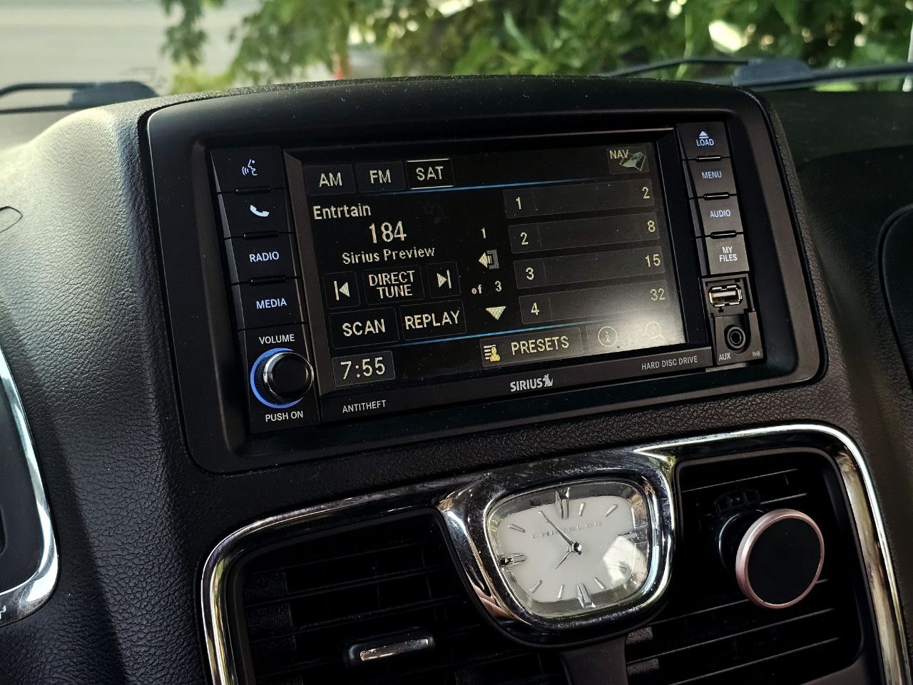 RV rental interior: infotainment system showing Sirius radio, navigation, and media options. Dashboard clock and phone mount visible.