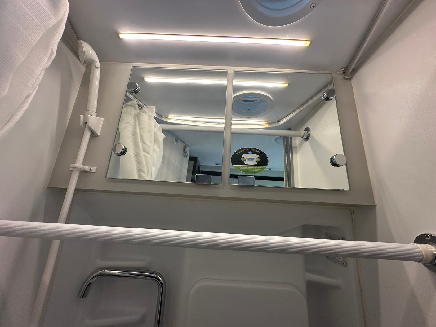 RV rental interior: compact shower/bathroom space with a mirror, shower head, and bright ceiling light.