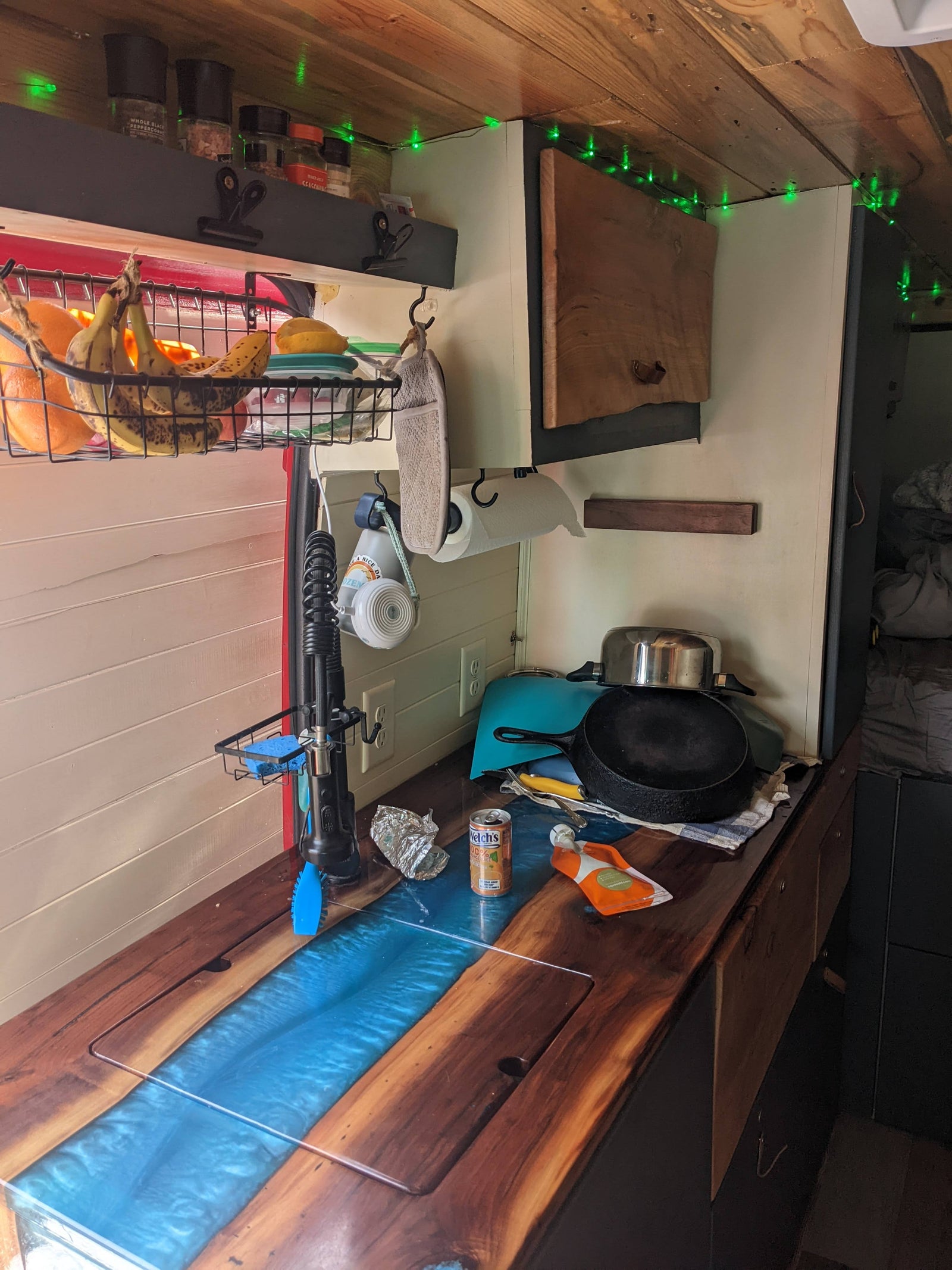 RV rental's cozy mobile kitchen: wood & resin countertop, fresh fruit, spices, cookware, and green lights.