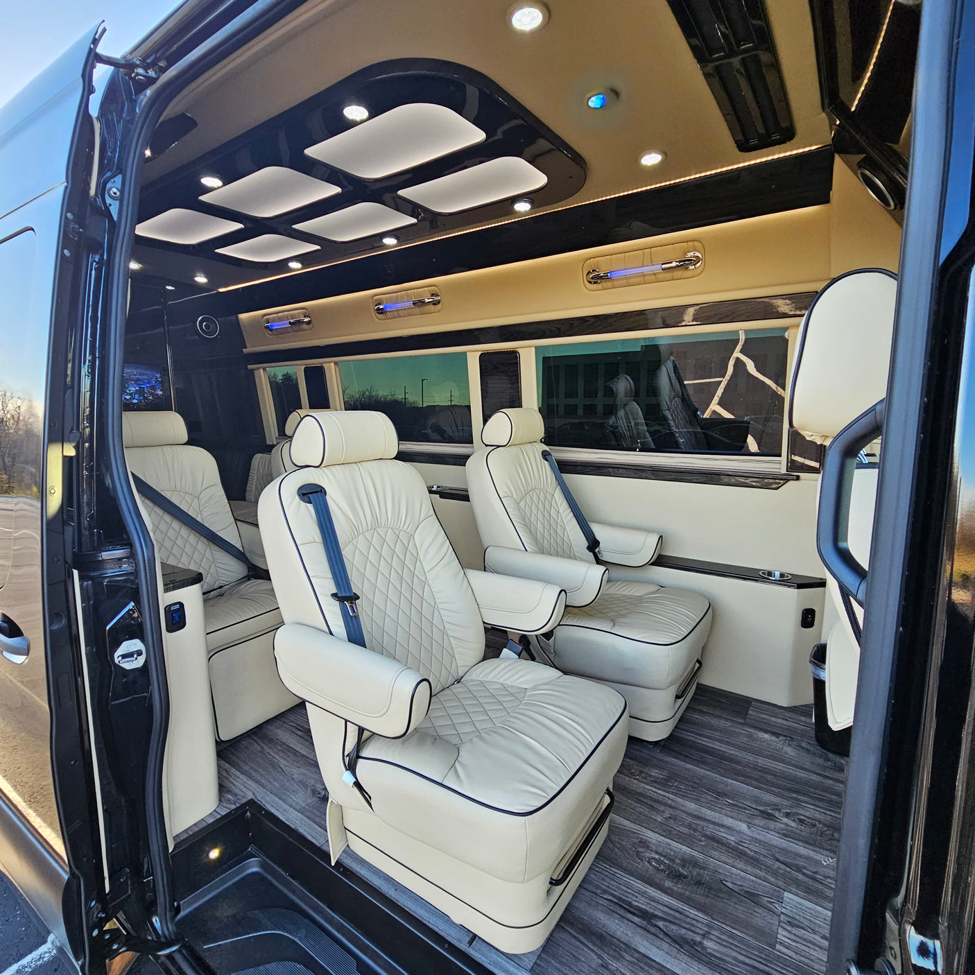 Luxury RV rental: spacious van interior featuring quilted cream seating, ambient lighting, and wood flooring.